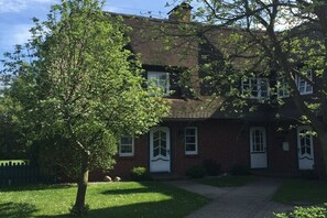 Een bakstenen huis met een witte deur en ramen, omringd door een gazon en een boom.
