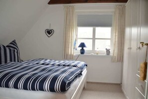 Een slaapkamer met een bed, een raam met gordijnen, een lamp en een hartvormige decoratie aan de muur.