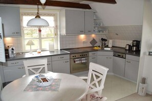 A kitchen with white cabinets, a stove, an oven, a sink, and a dining table with chairs. - House Bornholm "Anemone" (Nieblum)