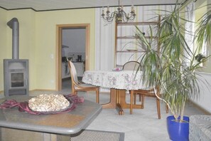 Un coin repas avec une table dressée pour deux personnes, une plante en pot et un poêle à bois.
