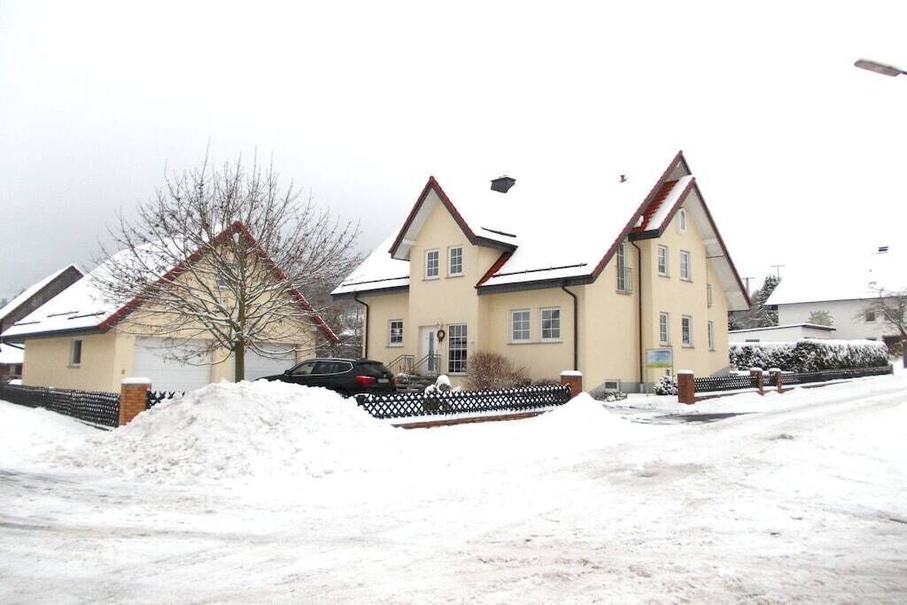 A residential building with a symmetrical facade, multiple windows, and a snow-covered ground.