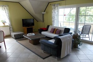 A living room with a sofa, a coffee table, a television, and a balcony with outdoor furniture. - Holiday apartment with 3 bedrooms (Ebersburg)