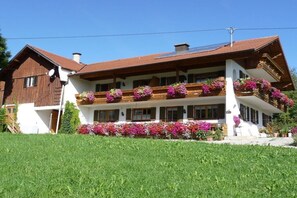 Un edificio de dos pisos con un balcón decorado con flores, fachada blanca y techo inclinado.