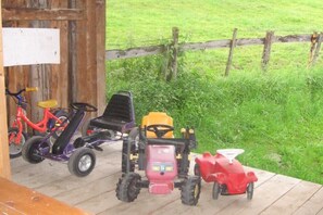 Eine Holzterrasse mit einem Schild, einem roten Spielzeugtraktor, einem violetten Spielzeugauto und einem roten Spielzeugmotorrad.