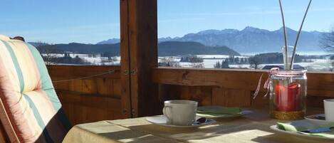 Une table avec une tasse et une soucoupe, une bougie dans un bocal et une vue sur les montagnes.