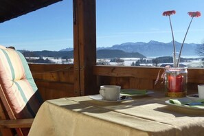 Una mesa con una taza y platillo, una vela en un frasco y vistas a las montañas.