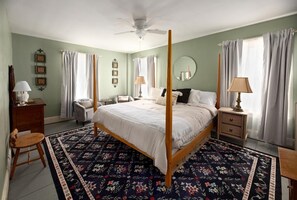 A four-poster bed with a floral-patterned rug, bedside tables, a chair, and a ceiling fan in a room with light green walls and curtains. - Historic Riders Hostelry (Painesville)