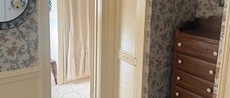 A room with floral wallpaper, a wooden dresser, and a door leading to a bathroom with a shower curtain.