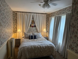A bedroom with a bed, two bedside lamps, a ceiling fan, and floral wallpaper. - Historic Riders Hostelry (Painesville)