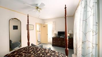 A bedroom with a four-poster bed, a ceiling fan, a dresser, a television, and a large mirror.