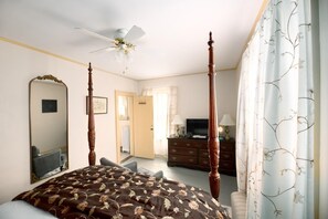A bedroom with a four-poster bed, a ceiling fan, a dresser, a television, and a large mirror. - Historic Riders Hostelry (Painesville)