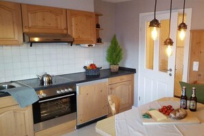 Une cuisine avec des meubles de rangement en bois, un four en acier inoxydable, un évier et un plan de travail agrémenté d’une plante et de bouteilles.