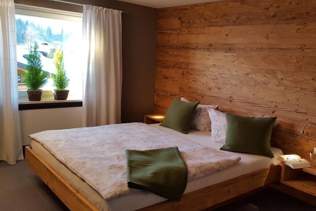 Une chambre à coucher avec une tête de lit en bois, un lit avec des coussins verts, une table de chevet avec une lampe et une fenêtre avec des rideaux.