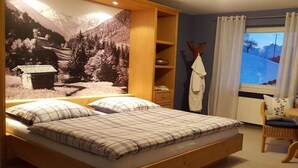 Quarto com cama, janela com cortinas, uma cadeira e parede com cena da natureza.