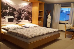 A bedroom with a bed, a window with curtains, a chair, and a wall with a nature scene. - Holiday apartment with 2 bedrooms (Sonthofen)