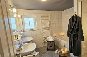 A bathroom with two sinks, a bathtub, a towel rack, and a robe hanging on the wall. - Holiday apartment with 2 bedrooms (Sonthofen)