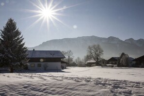 A snow-covered landscape with a house and mountains in the background.