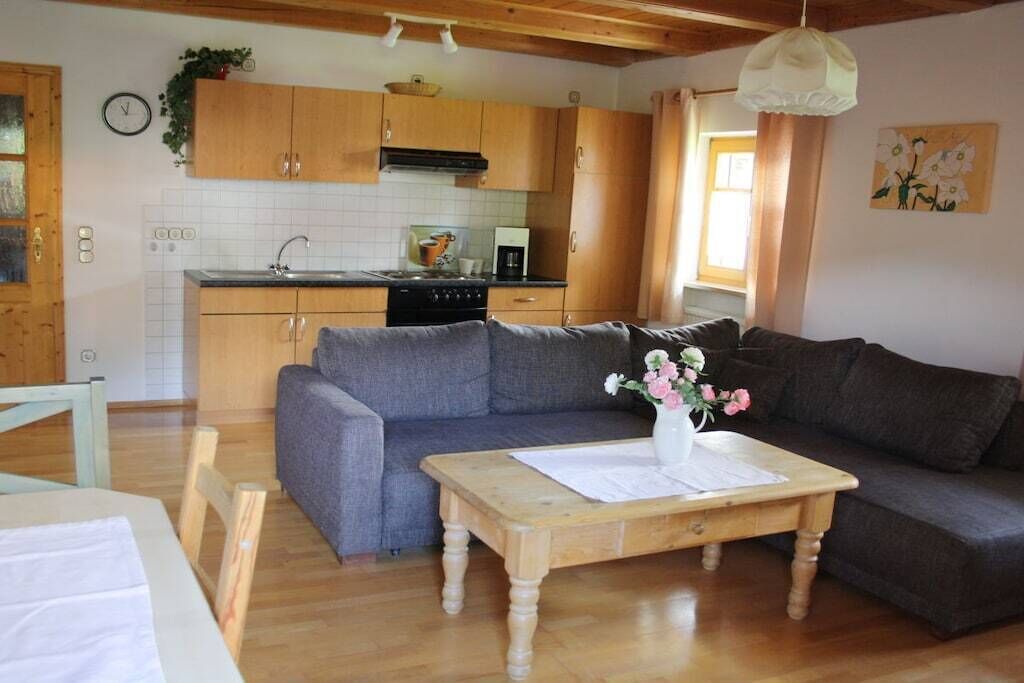 A compact living space with a kitchenette, a grey sofa, a wooden coffee table, and a vase of flowers.