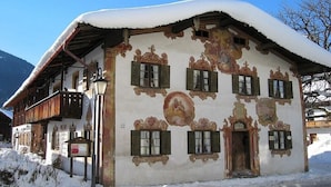Um edifício coberto de neve com arquitetura tradicional, incluindo uma varanda e uma porta com moldura de madeira.