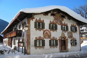 Un bâtiment recouvert de neige, doté d’une architecture traditionnelle, comprenant un balcon et une porte avec un cadre en bois.