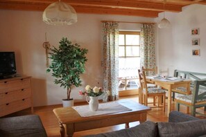 Un salon chaleureux avec un banc en bois, une plante en pot et un coin repas comprenant une table et des chaises.