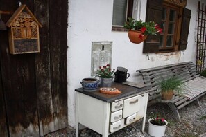 A rustic outdoor setting with a wooden bench, a white cabinet with drawers, a hanging birdhouse, and potted plants. - Holiday apartment with 1 bedroom (Unterammergau)