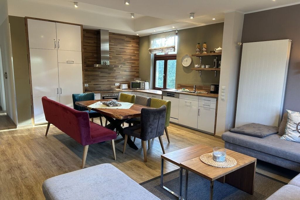 Een moderne keuken met houten kasten, een eethoek met een tafel en stoelen, en een zithoek met een bank.