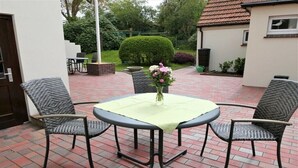 An outdoor patio with a round table and four chairs, a vase with flowers, and a brick floor. - Holiday apartment with 4 bedrooms (Wangerooge)