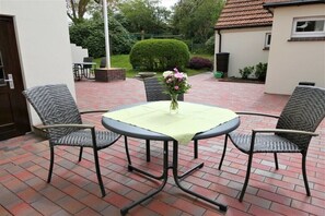 Una terrazza esterna con un tavolo rotondo e quattro sedie, un vaso con fiori e un pavimento in mattoni.