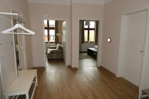 A room with a wooden floor, a white bench, a hanging coat rack, and a door leading to another room. - Holiday apartment with 4 bedrooms (Wangerooge)