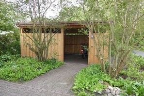 A wooden structure with a covered entrance, surrounded by lush greenery and a paved pathway. - Holiday apartment with 4 bedrooms (Wangerooge)
