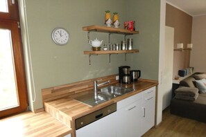 A compact kitchen with a wooden countertop, stainless steel sink, and white cabinets. There is a clock on the wall and a shelf with kitchen items. - Holiday apartment with 4 bedrooms (Wangerooge)