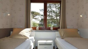 A room with two beds, a radiator, and a window with a view of trees. - Holiday apartment with 4 bedrooms (Wangerooge)