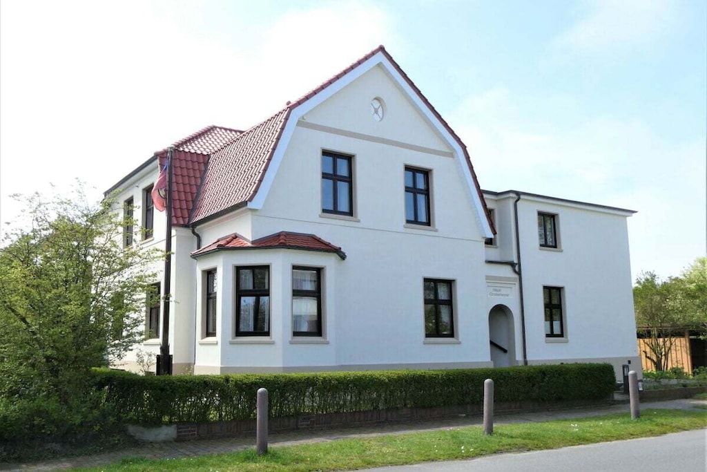 Un bâtiment blanc à deux étages, avec un toit recouvert de tuiles rouges, de nombreuses fenêtres et une petite entrée.