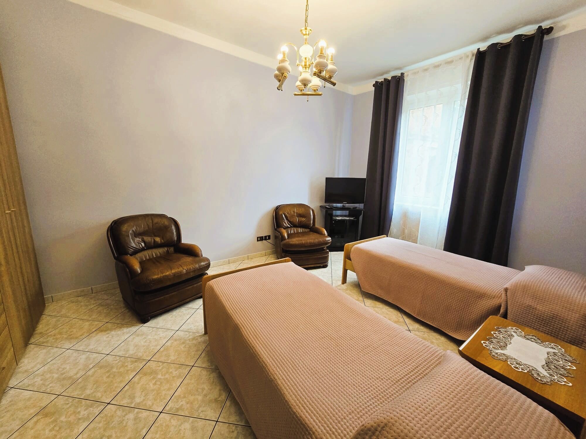 A hotel room with two beds, a sofa, a TV, and a chandelier.