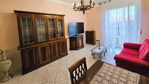 A living room with a wooden cabinet, a television, a red sofa, and a chandelier. - Galileo Ferraris Apartment, Short-Term Rentals in the City of Vercelli (Vercelli)
