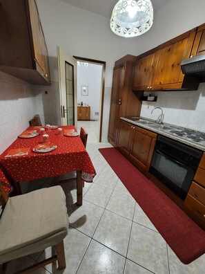 A compact kitchen with wooden cabinets, a dining table set for four, and a red rug. - Galileo Ferraris Apartment, Short-Term Rentals in the City of Vercelli (Vercelli)