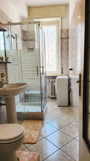 Un bagno con doccia vetrata, lavandino, WC e termosifone.