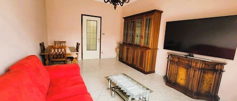 A living room with a red sofa, a television, a cabinet, and a chandelier.