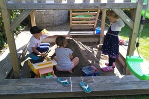 A wooden play structure with a sandbox, a small table, and a swing. - Wiesenblick - Family Herb (Rettenberg)