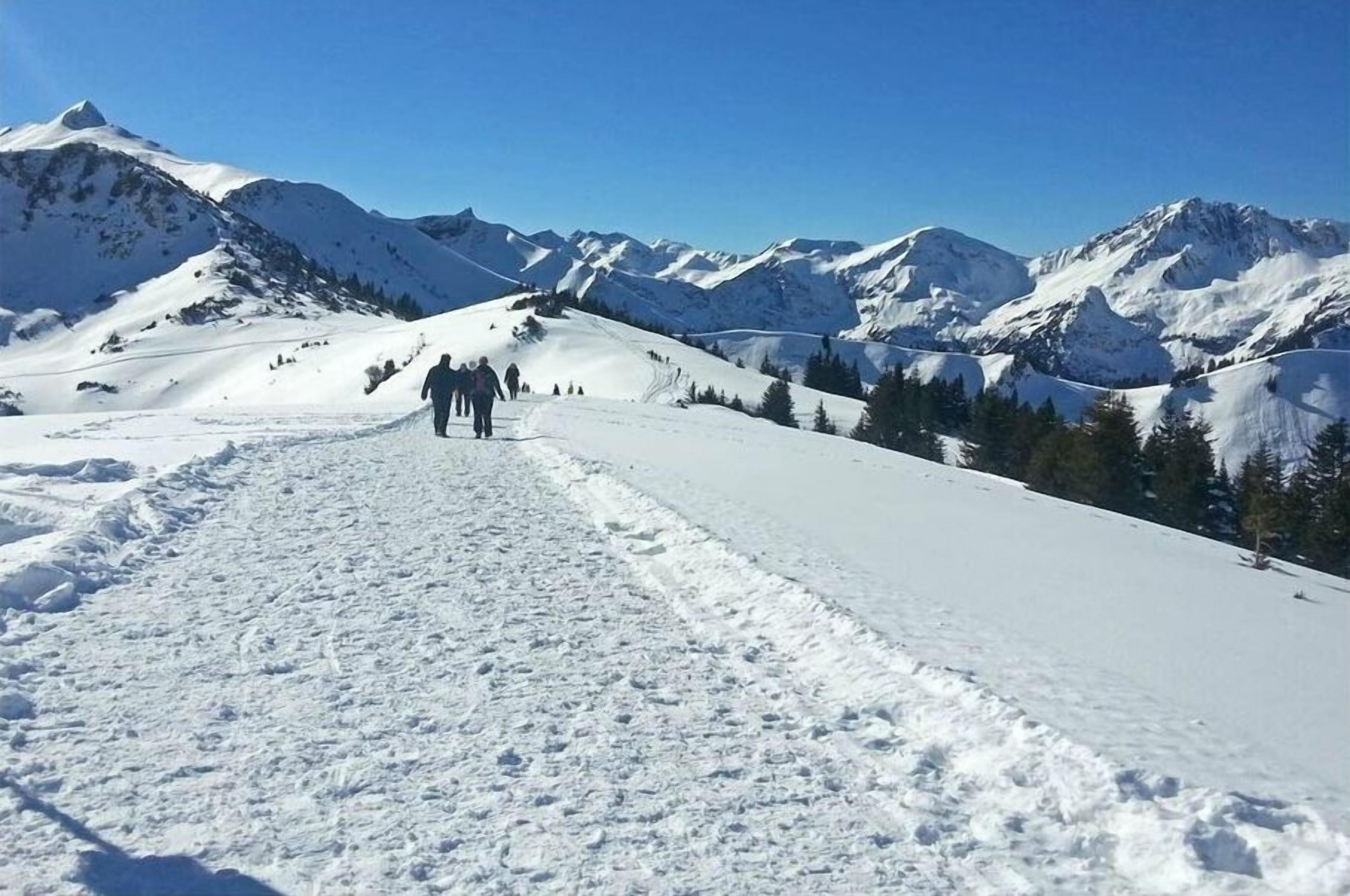A snow-covered mountain path with a clear sky and distant mountains.