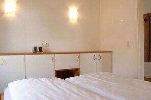 Une chambre d’hôtel avec deux lits, une tête de lit en bois, une petite étagère avec quelques objets et des lampes fixées au mur.