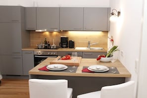 A compact kitchen with grey cabinets, a wooden countertop, and a small dining area with two white chairs. - Holiday apartment with 2 bedrooms (Chieming)