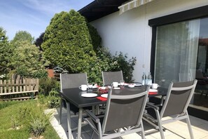 An outdoor patio with a table set for four, surrounded by chairs, and a wooden fence in the background. - Holiday apartment with 2 bedrooms (Chieming)