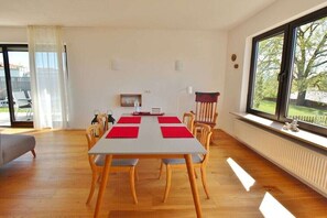 A dining area with a table set for four, wooden chairs, a sofa, and a window with a view of greenery. - Holiday apartment with 2 bedrooms (Chieming)
