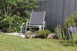 Un jardin avec une chaise en métal, un banc en bois et diverses plantes.