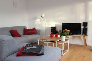 A modern living room with a grey sofa, red cushions, a white coffee table, a flat-screen TV, speakers, and a potted plant. - Holiday apartment with 2 bedrooms (Chieming)