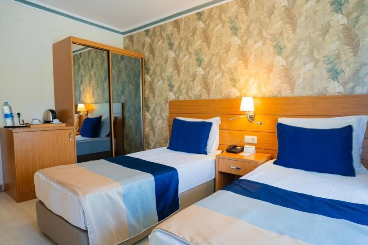 Une chambre d’hôtel avec deux lits, une armoire, une table de chevet avec une lampe et un miroir.
