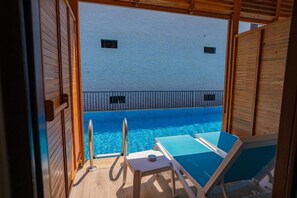 A poolside area with two lounge chairs and a small table, a wooden deck, and a white building with a blue pool in the background. - Master Family Club Hotel - All Inclusive (Manavgat)