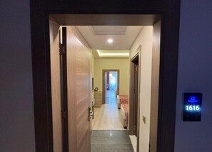 Un couloir d’hôtel avec un panneau numérique indiquant le numéro de chambre, un lit et une salle de bain.